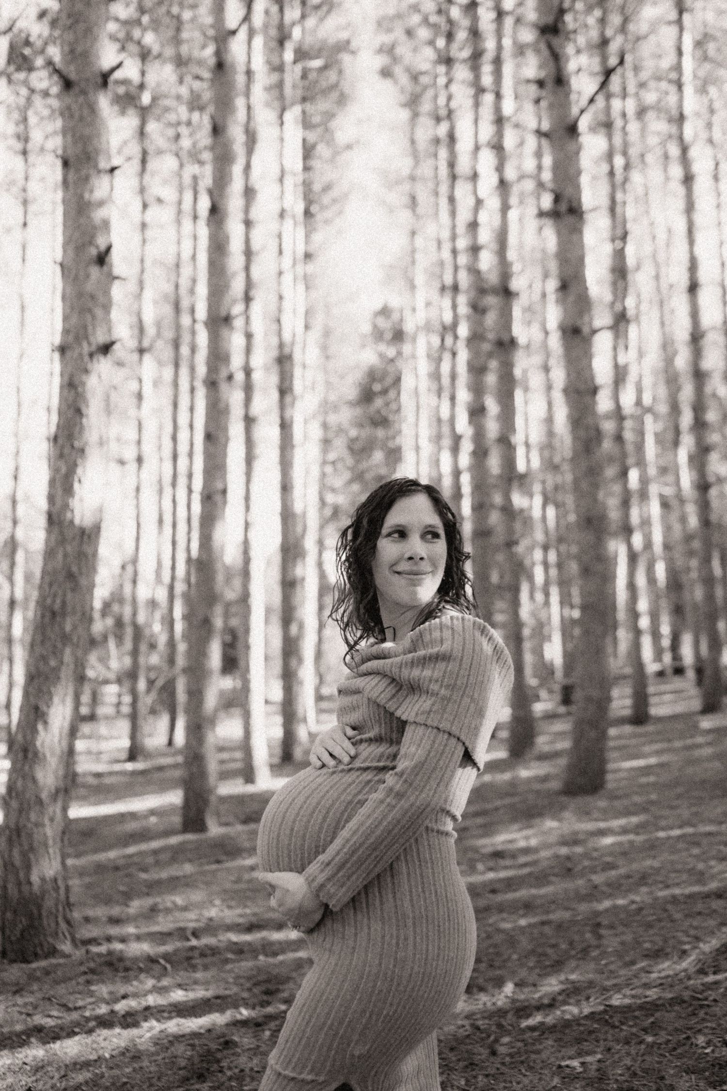 A series of maternity photos showing a woman in a sweater posing in a sunlit forest.