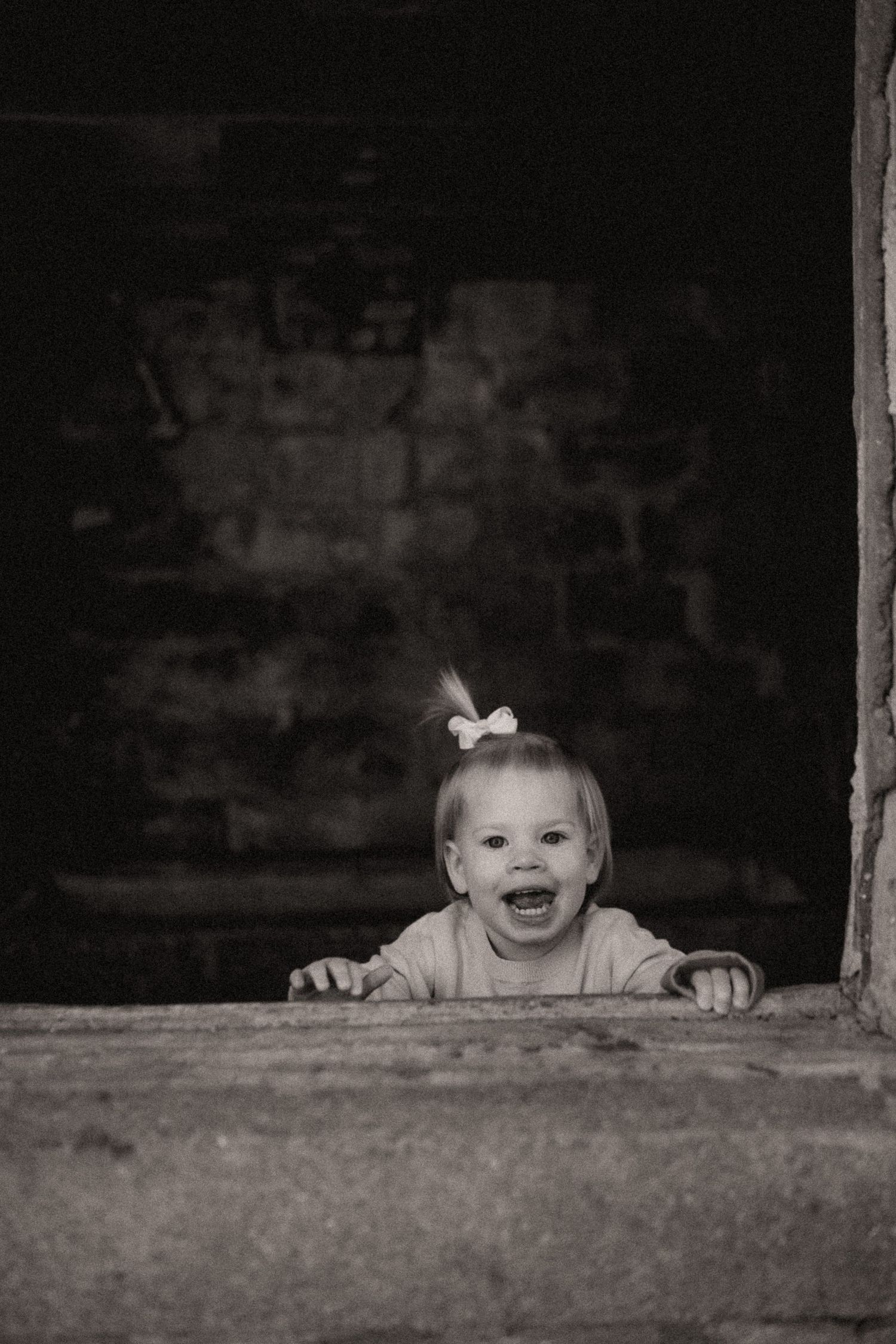 Black and white photos showing playful peekaboo moments through a rustic window frame.