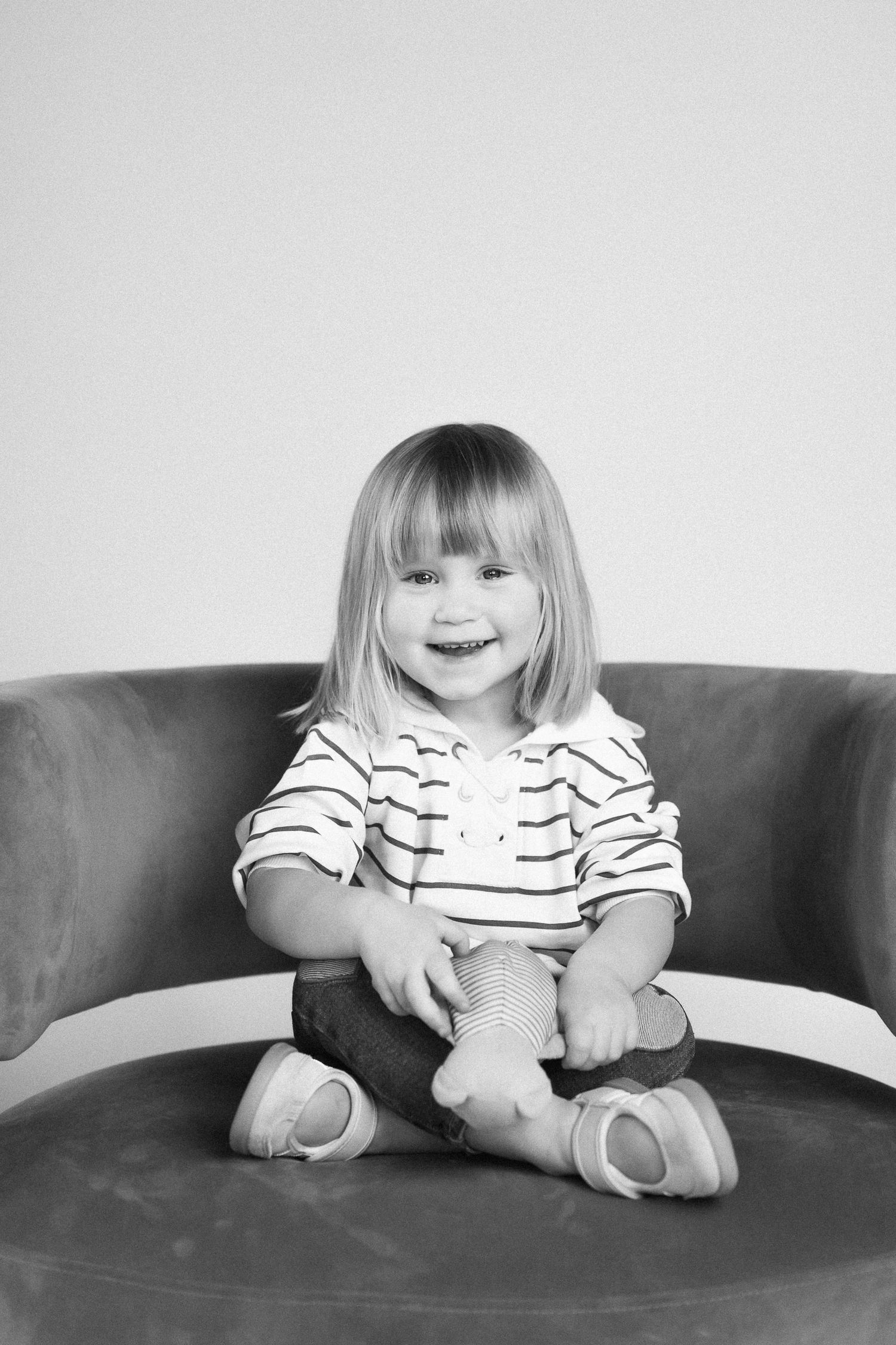 Black and white photo series showing a small child in a striped shirt sitting and laughing on a dark couch.