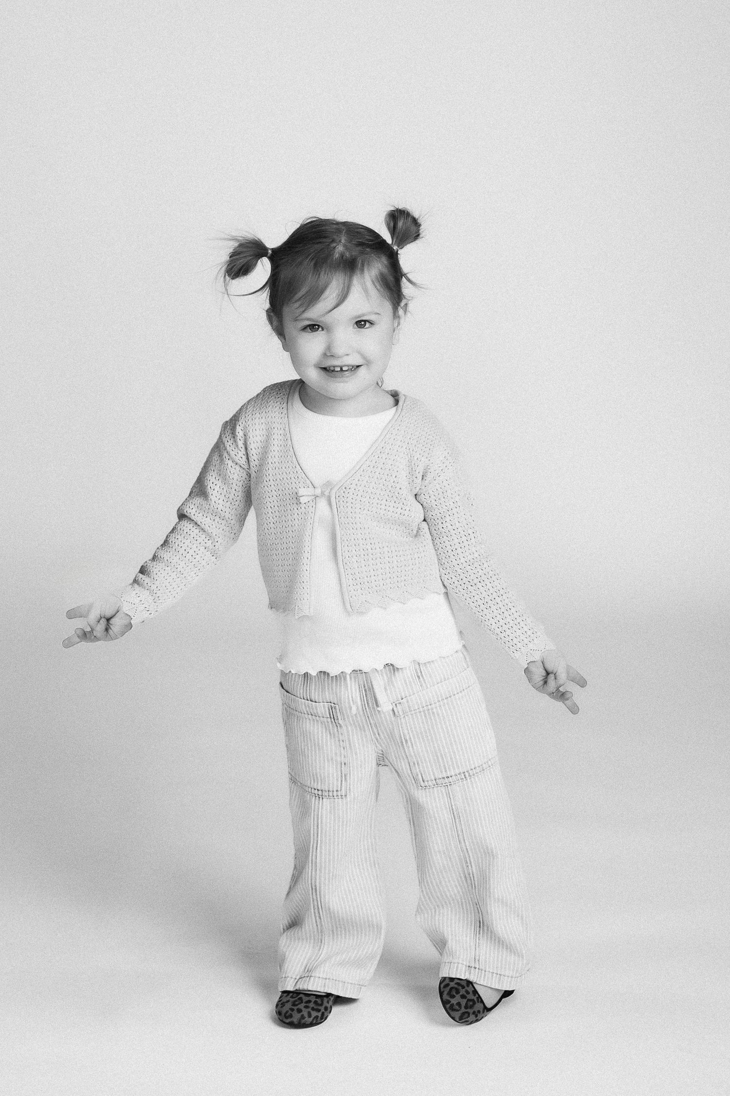 Playful black and white portraits of toddler in light colored overalls showing different poses and expressions.