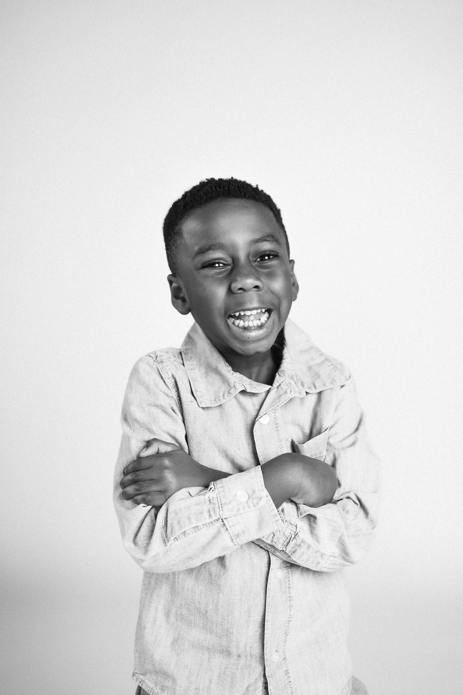 A young child in a white shirt laughs joyfully while hugging themselves against a light background.
