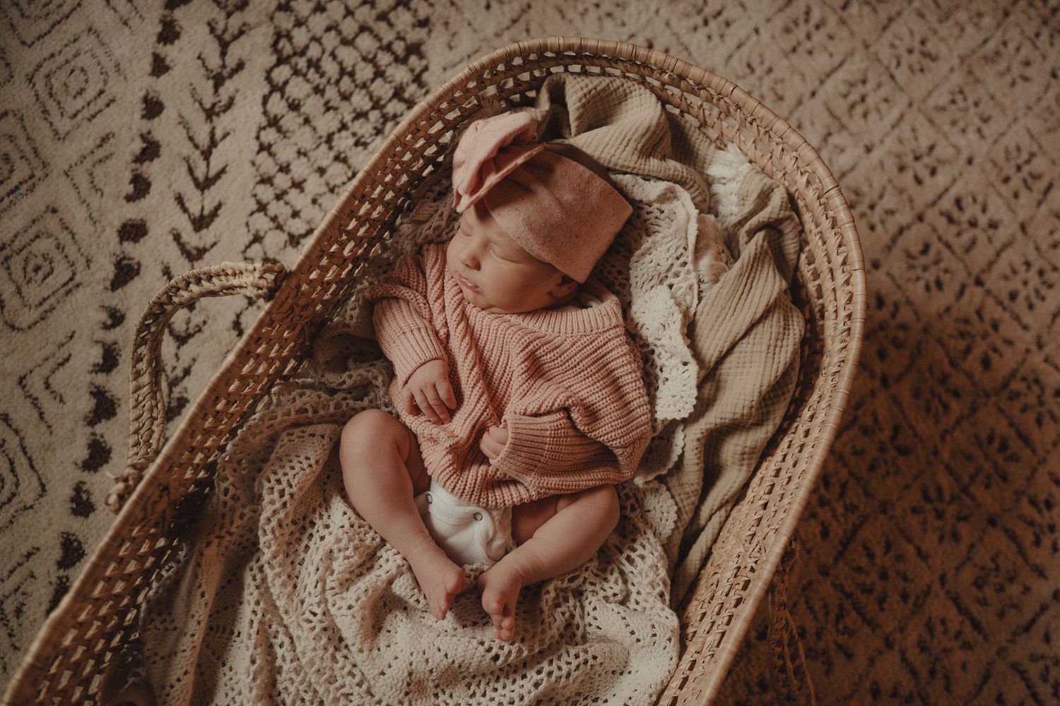 A delicate pink newborn outfit laid out on intricate patterned fabric.