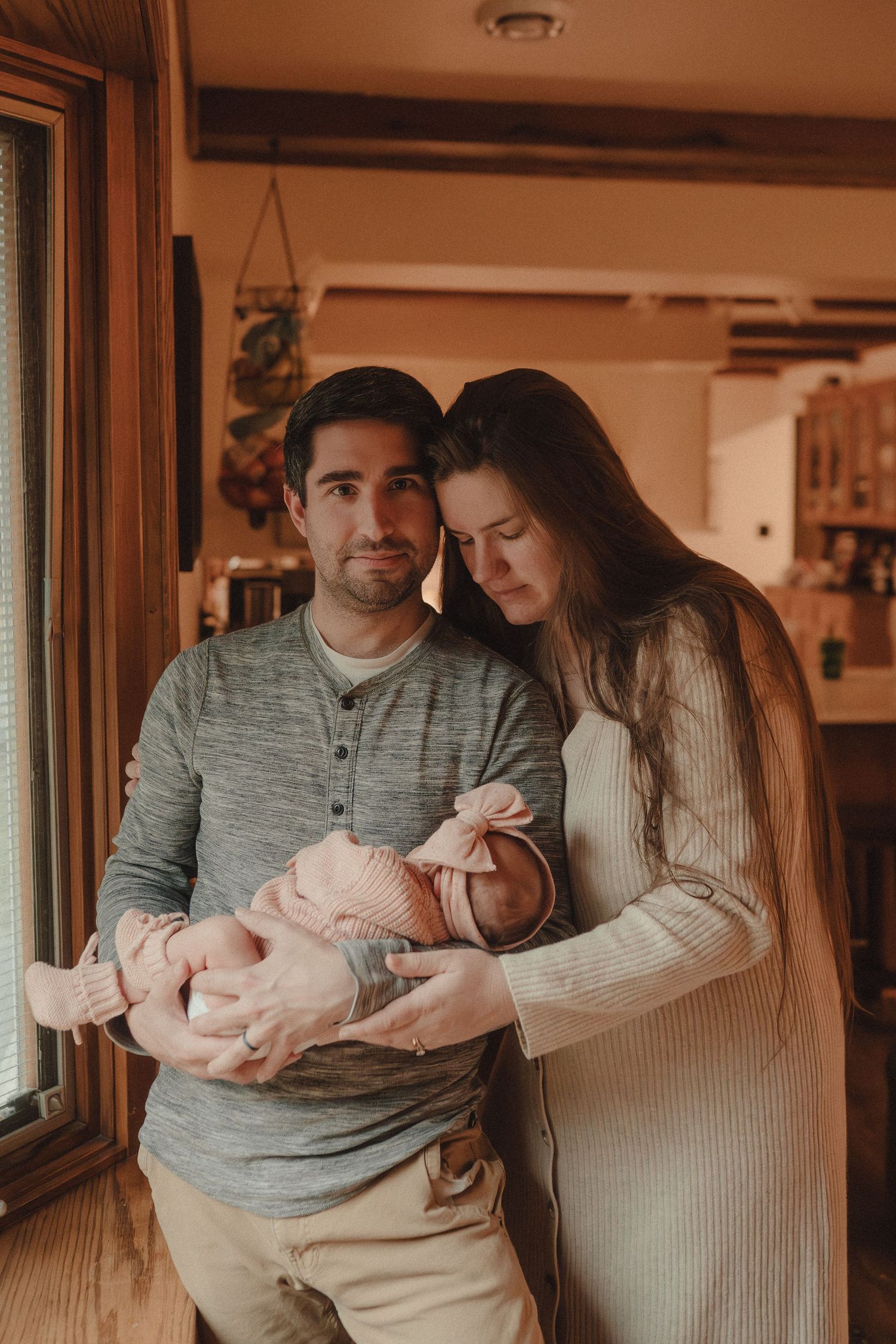 An intimate family moment captured in warm tones as they gather near a window.