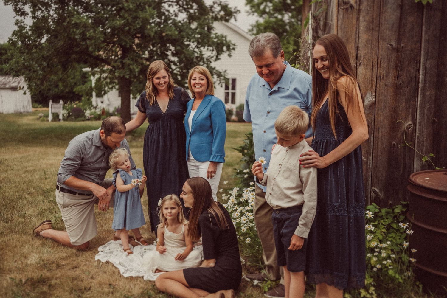 Family portrait taken outside weathered barn with greenery in background.