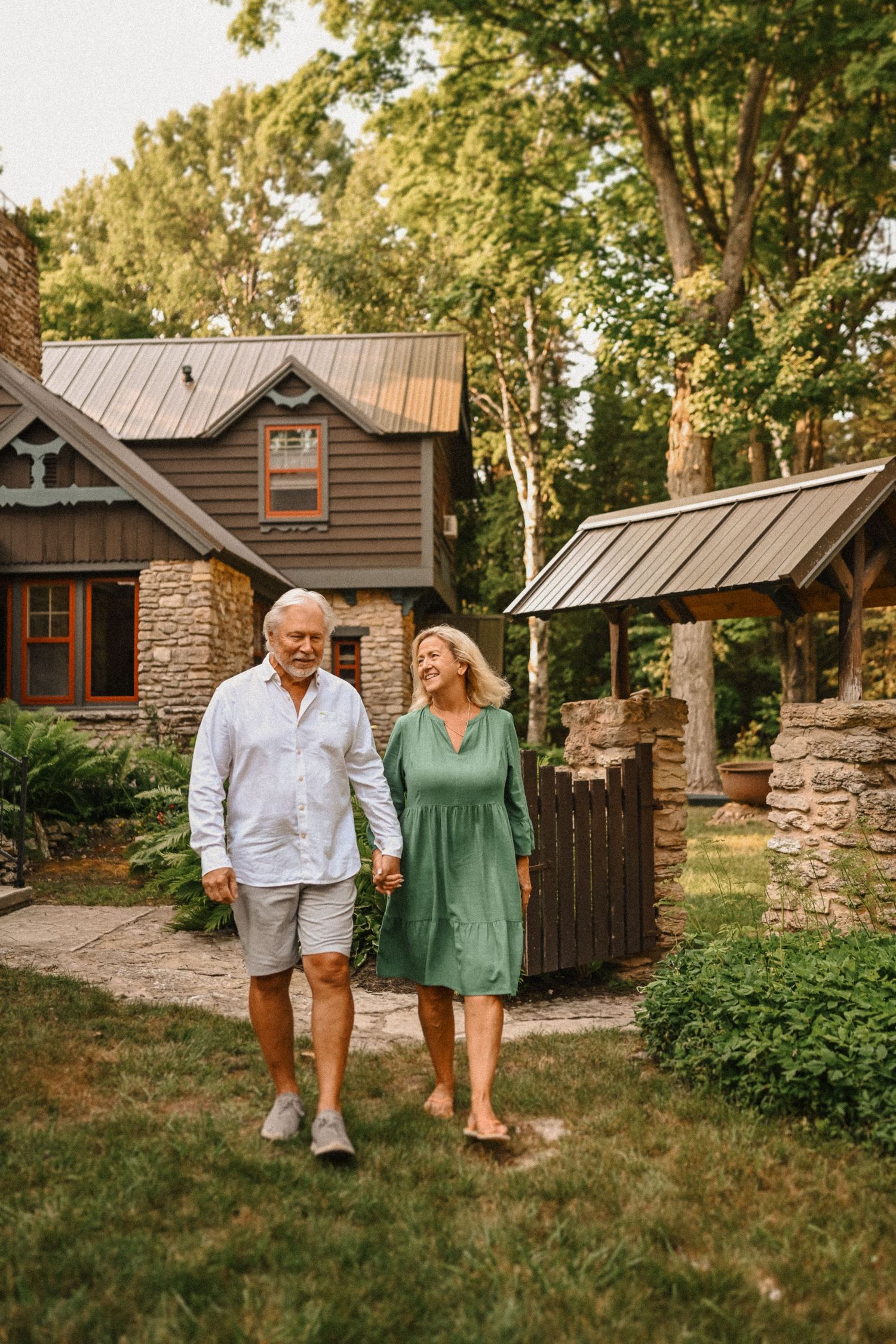 Couple strolling together outside charming cottage with stone facade and metal roof.
