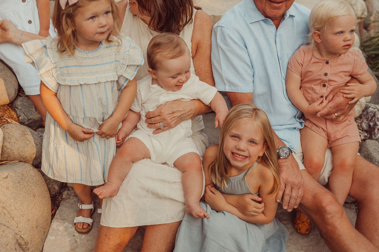Close-up of children and adults sitting together on decorative rocks in soft lighting.