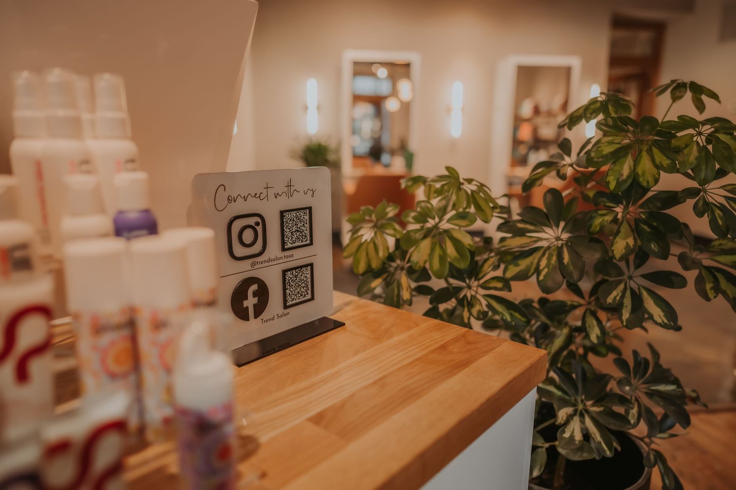Retail display corner with social media signage and decorative plants in modern salon setting.