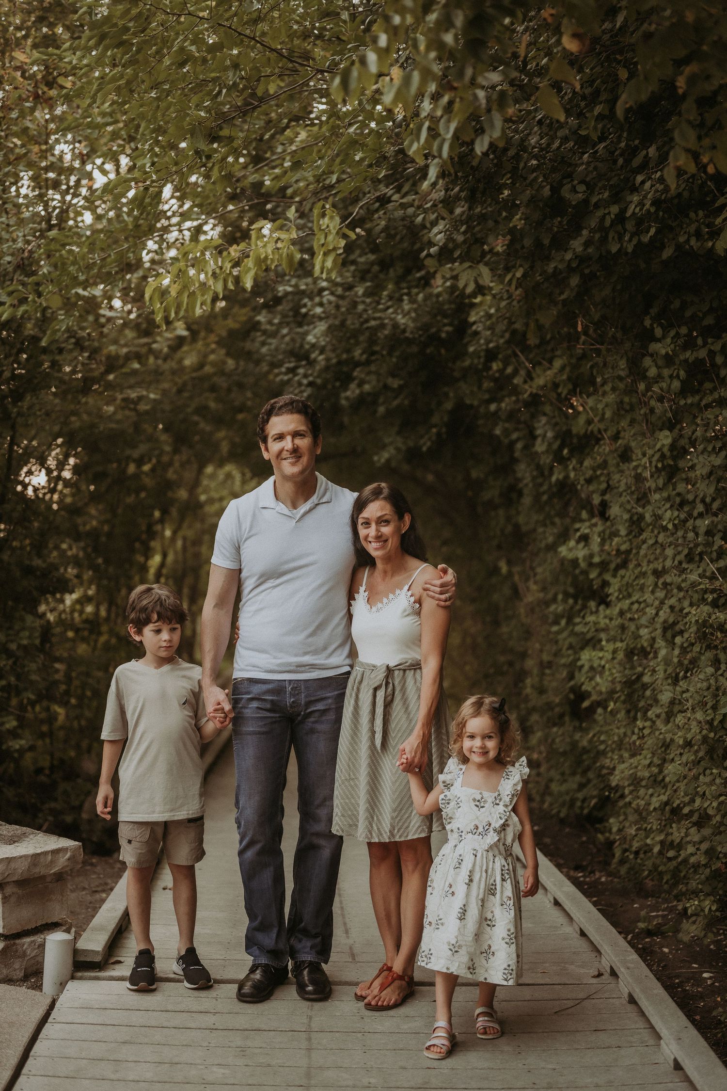 A family of four stands together on a wooden boardwalk during a warm sunset photoshoot.