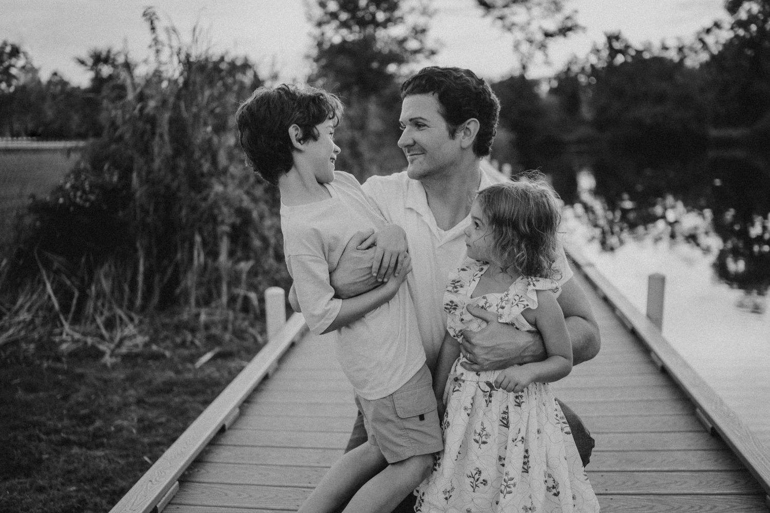 Black and white capture of a loving family moment on a wooden boardwalk.