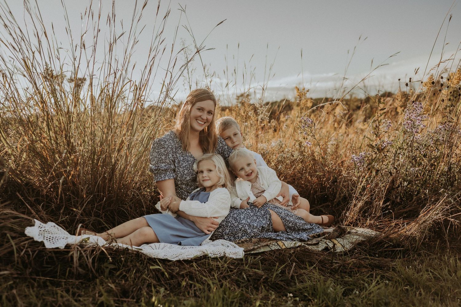 Family relaxing on picnic blanket surrounded by golden autumn grass at sunset.
