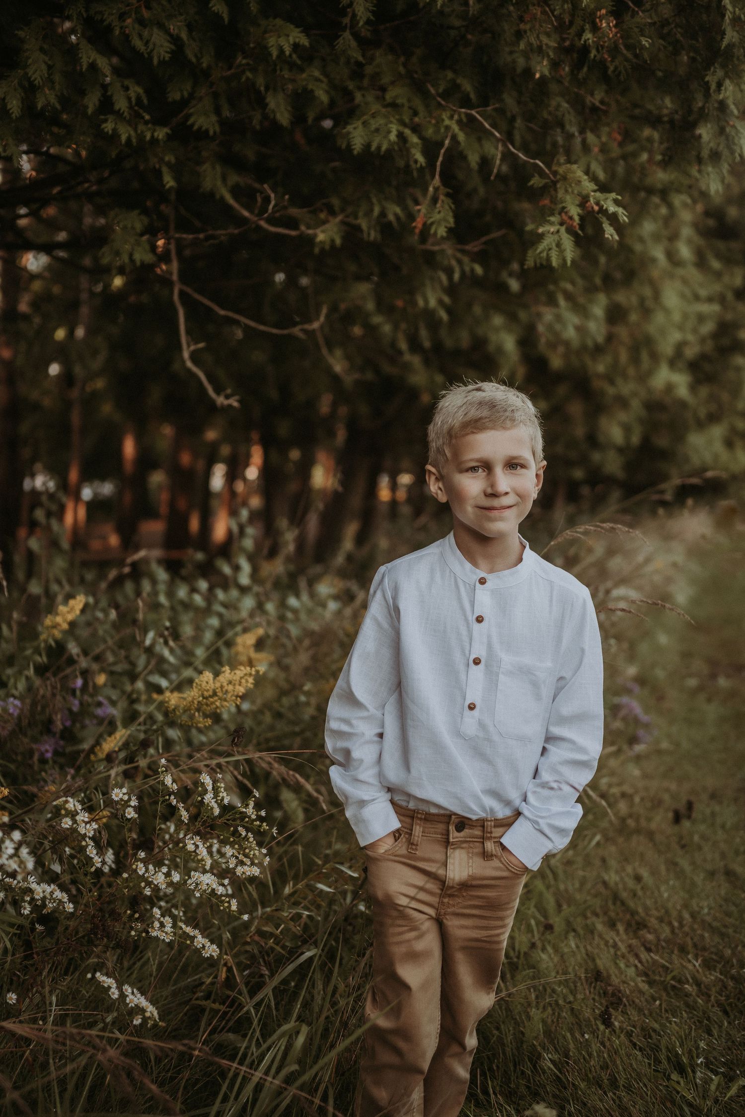 Portrait of a child in a white henley shirt and khaki pants standing in a natural outdoor setting at golden hour.