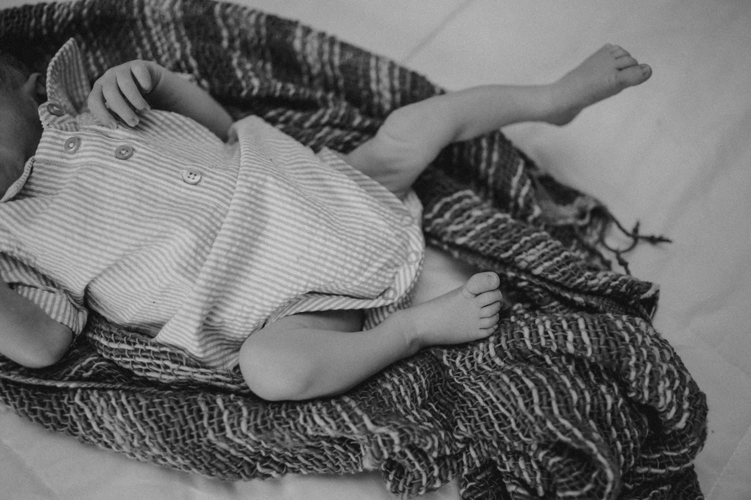 Black and white photo of infant sleeping on cozy striped blanket.
