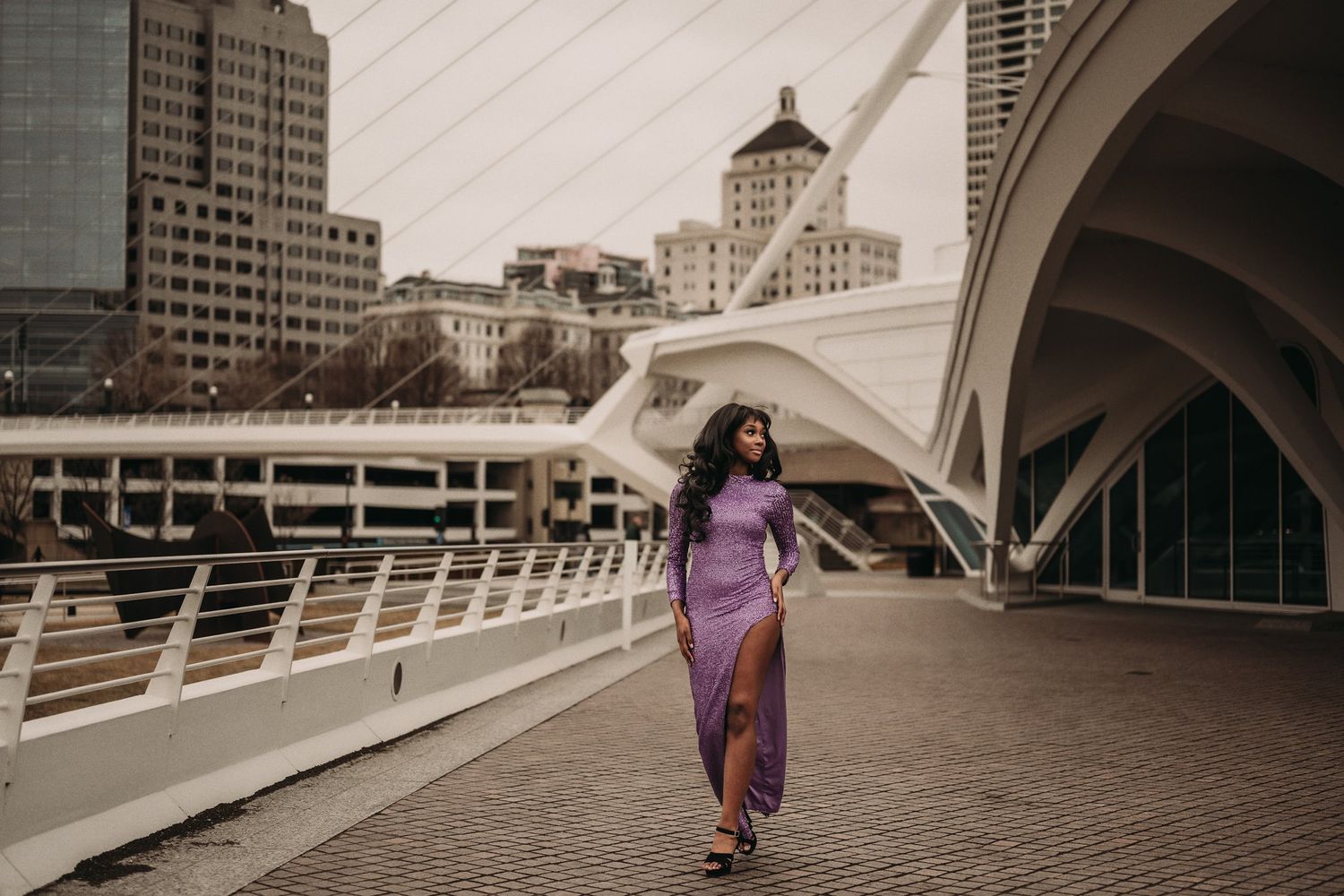 Artistic fashion photograph with flowing purple dress against architectural backdrop.