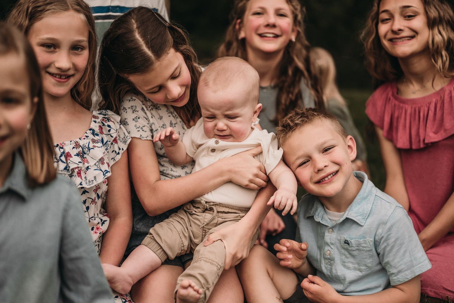 A group of children gather closely around a baby, sharing laughter and smiles in a candid moment.
