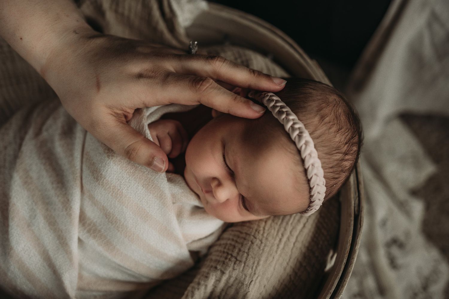 A sleeping newborn wearing a delicate headband is gently touched by caring hands.