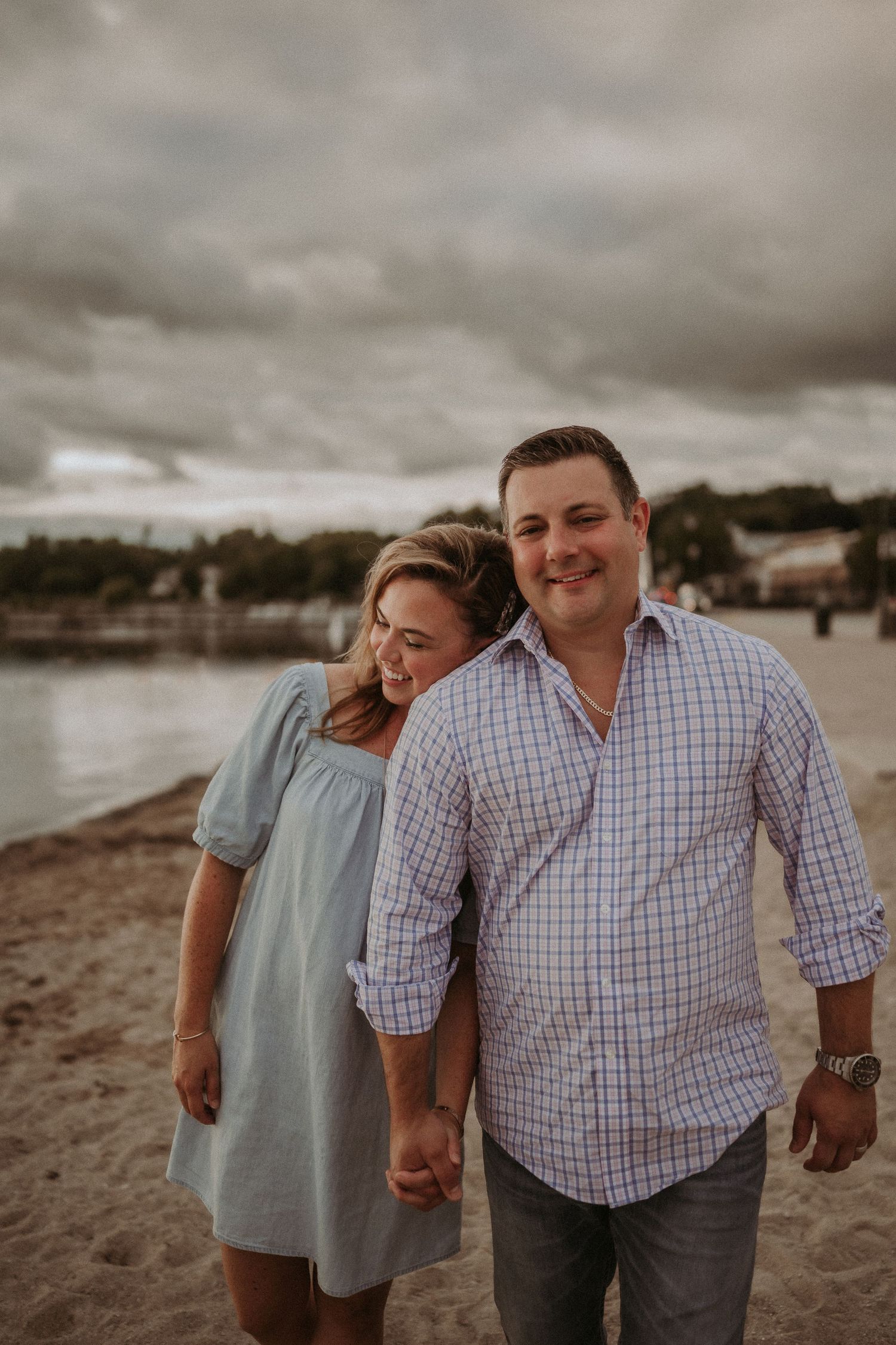A couple shares an intimate moment on a beach with moody storm clouds overhead.