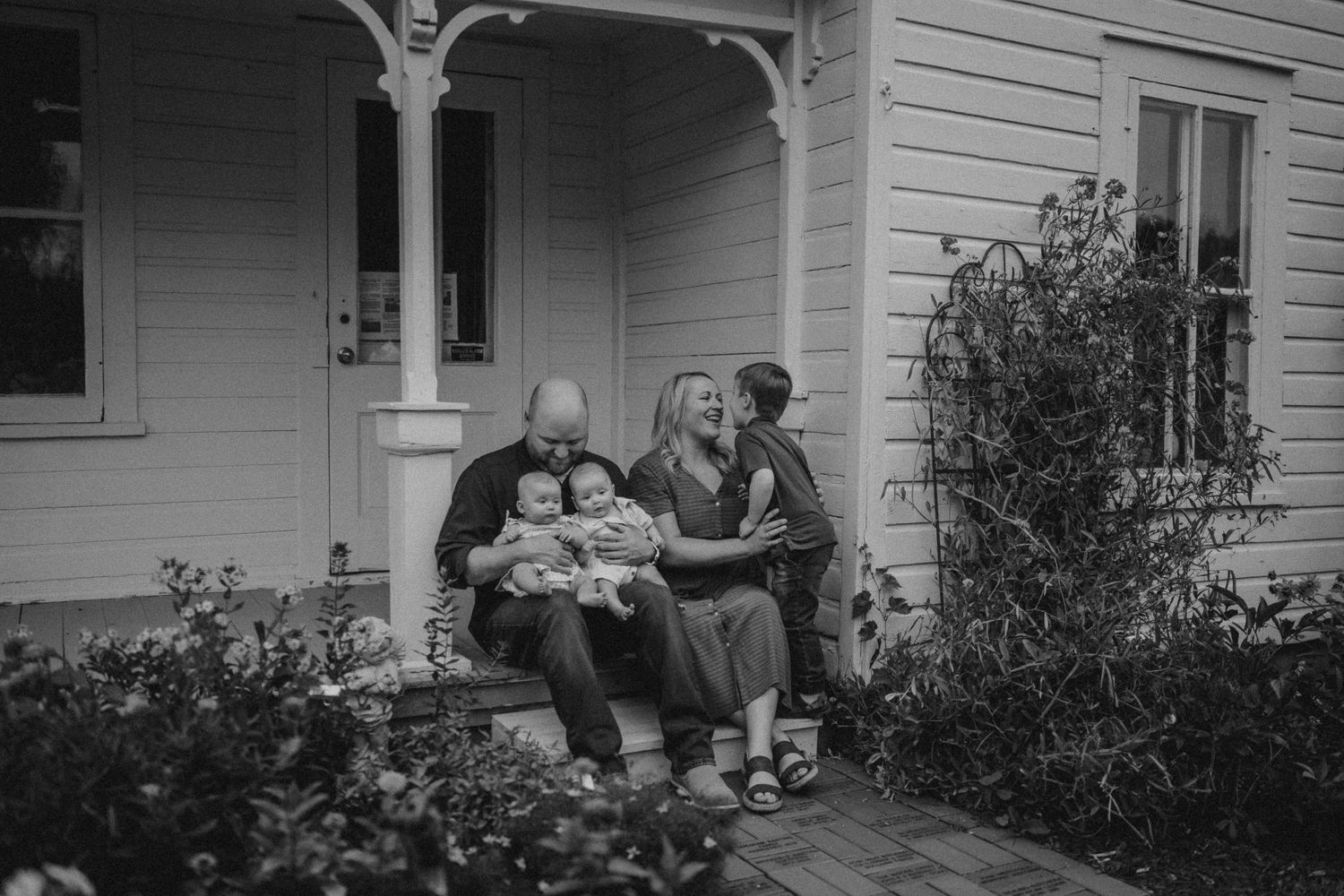 Black and white portrait of a family sitting together on porch steps of a vintage farmhouse.