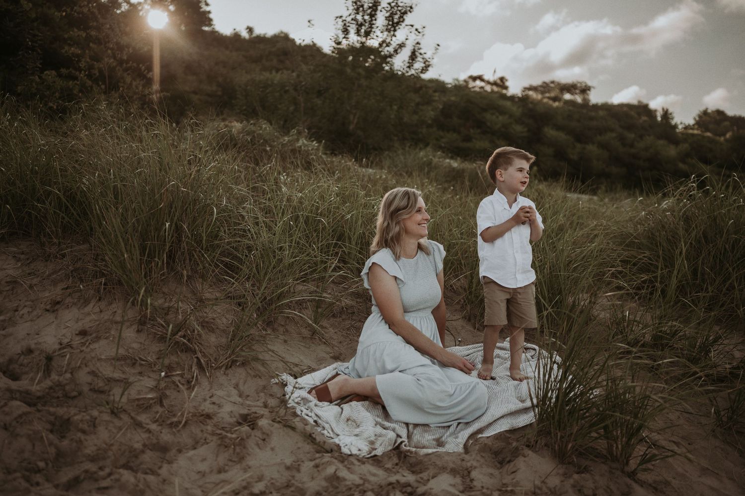 A sunset photoshoot in tall grass with two people sitting on a blanket.