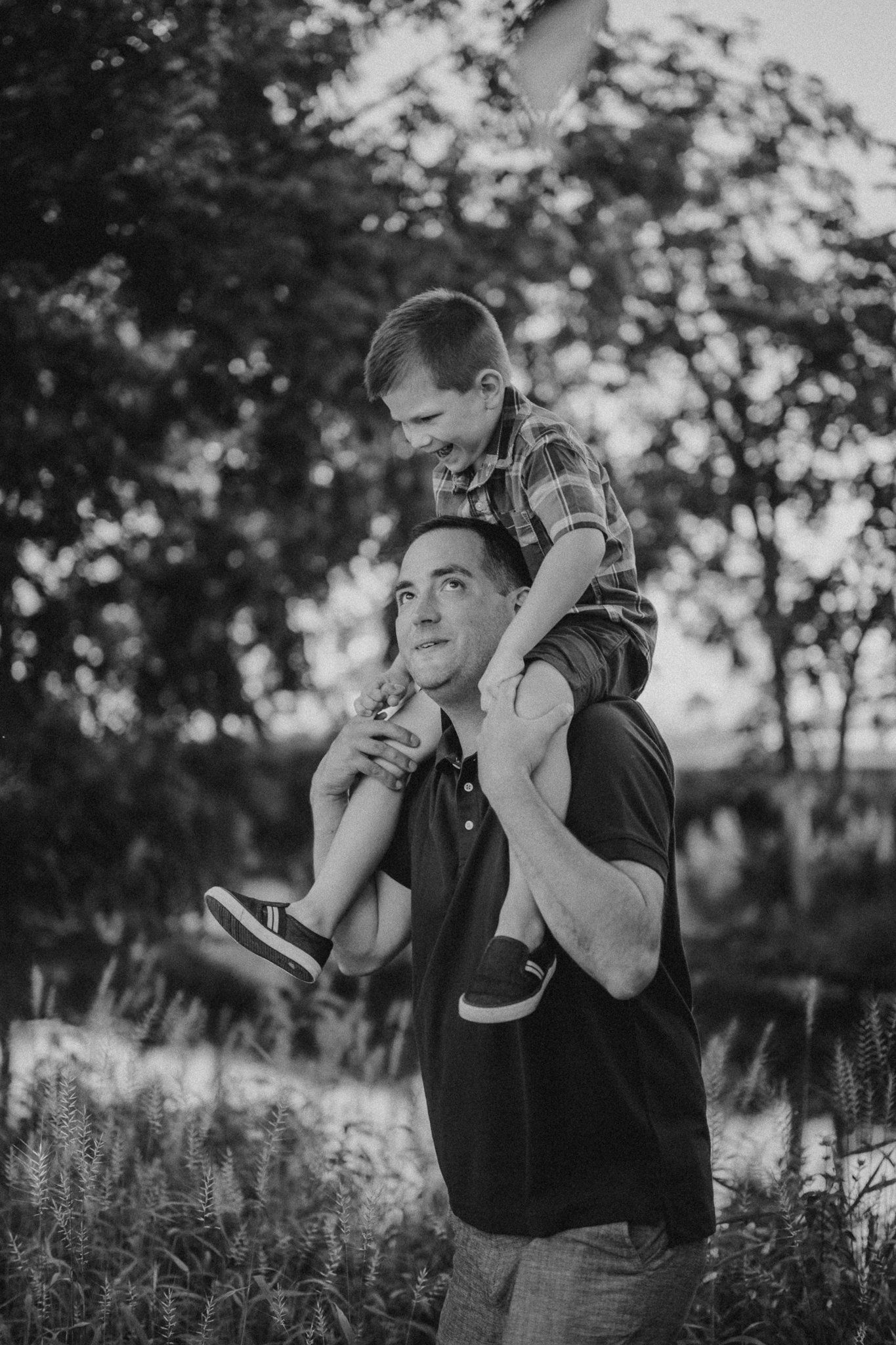 A tender moment captured in black and white as a child rides on someone's shoulders in nature.