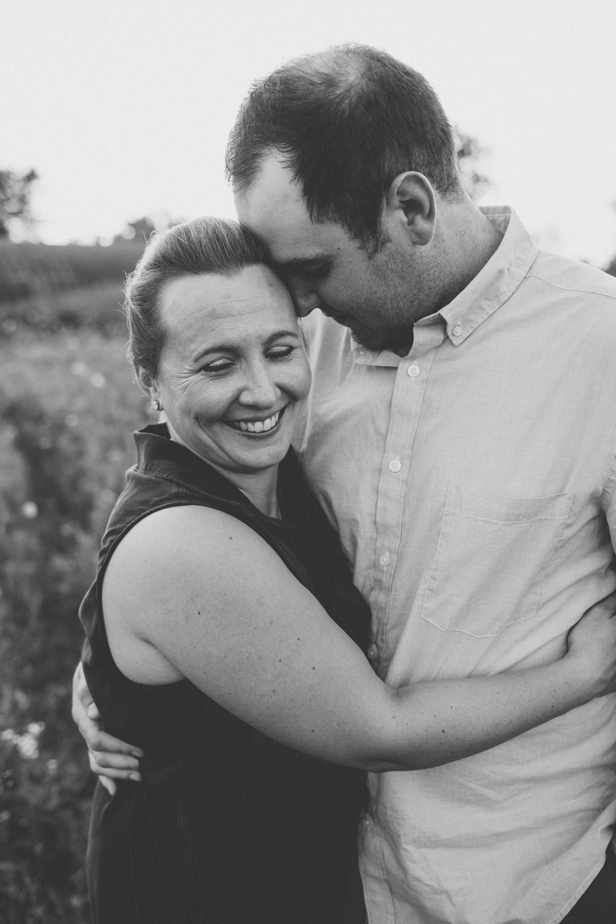 A black and white portrait of a couple embracing and laughing in an outdoor setting.