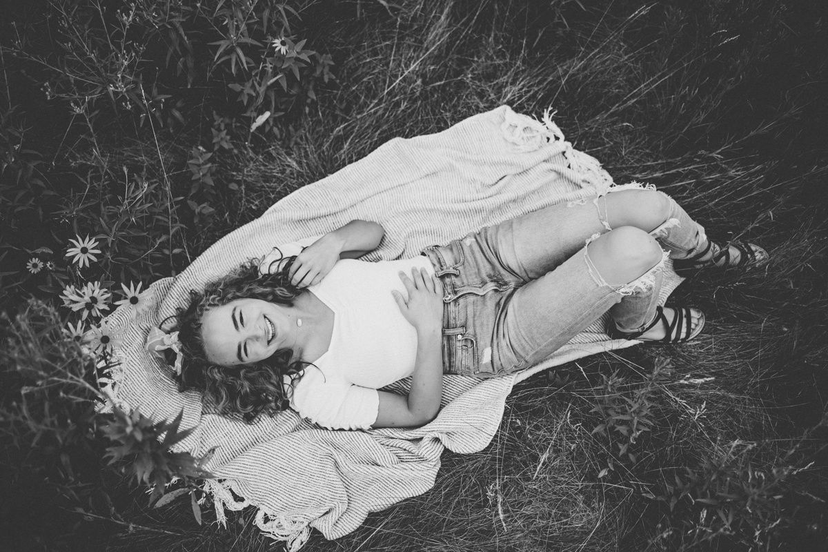 Black and white image of someone reclining on blanket in wildflower field.