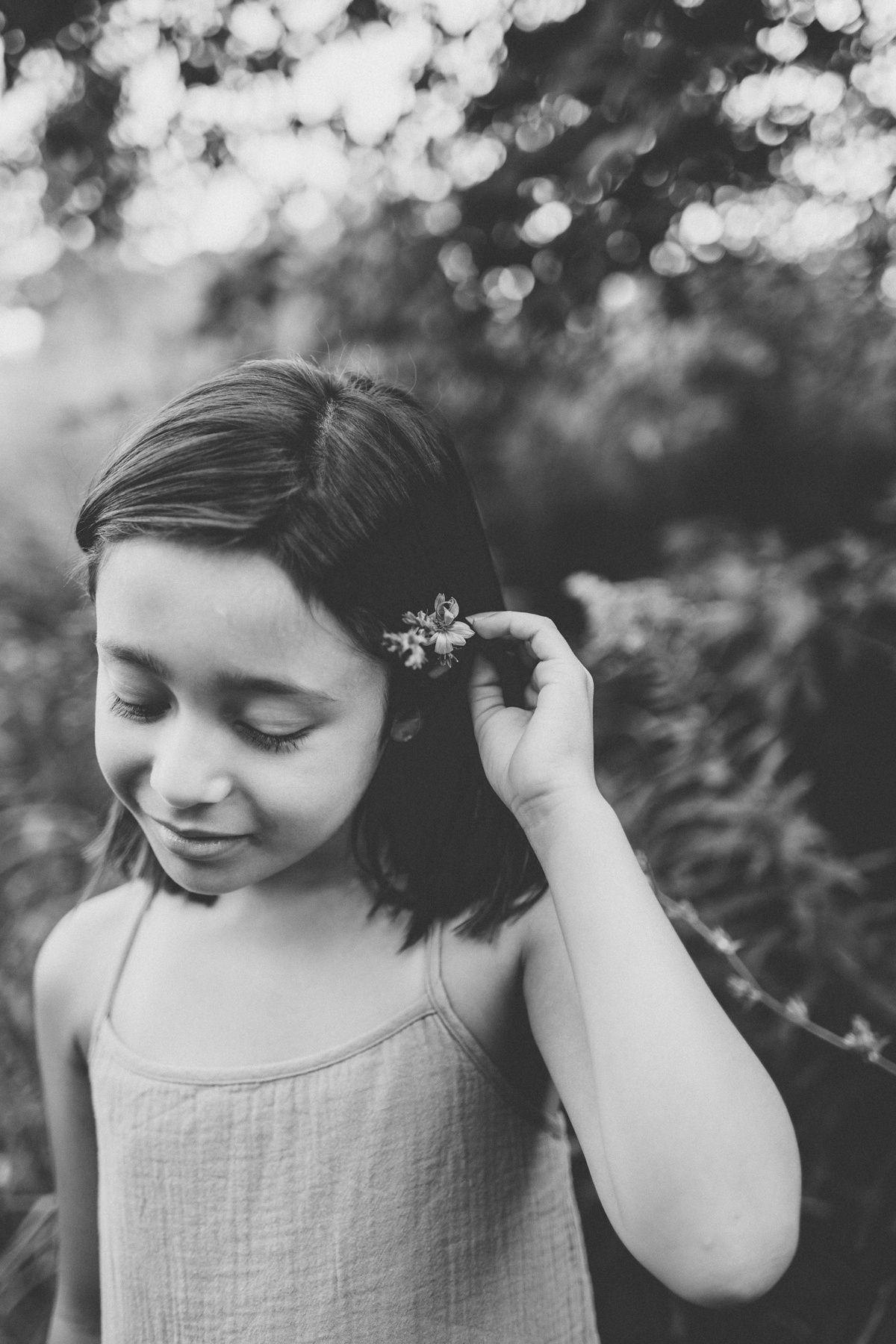 Black and white portrait showing someone placing a flower in their hair with dreamy bokeh.