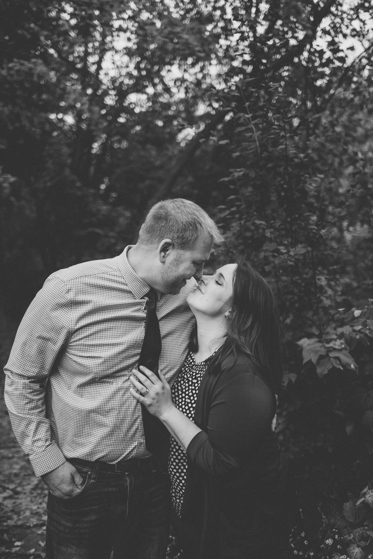 Black and white intimate portrait of couple sharing tender moment in forest setting.