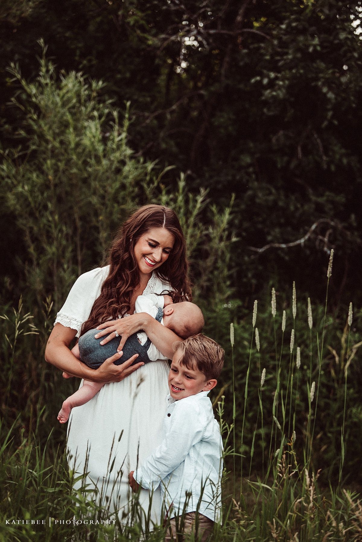 Tender family moment captured in a natural outdoor setting with tall grass and greenery.