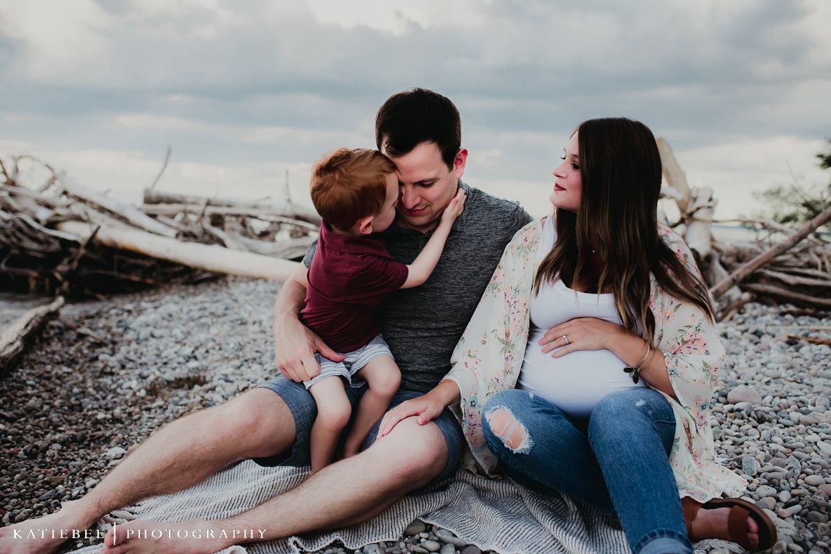 A casual family portrait session on a beach with driftwood and overcast skies.