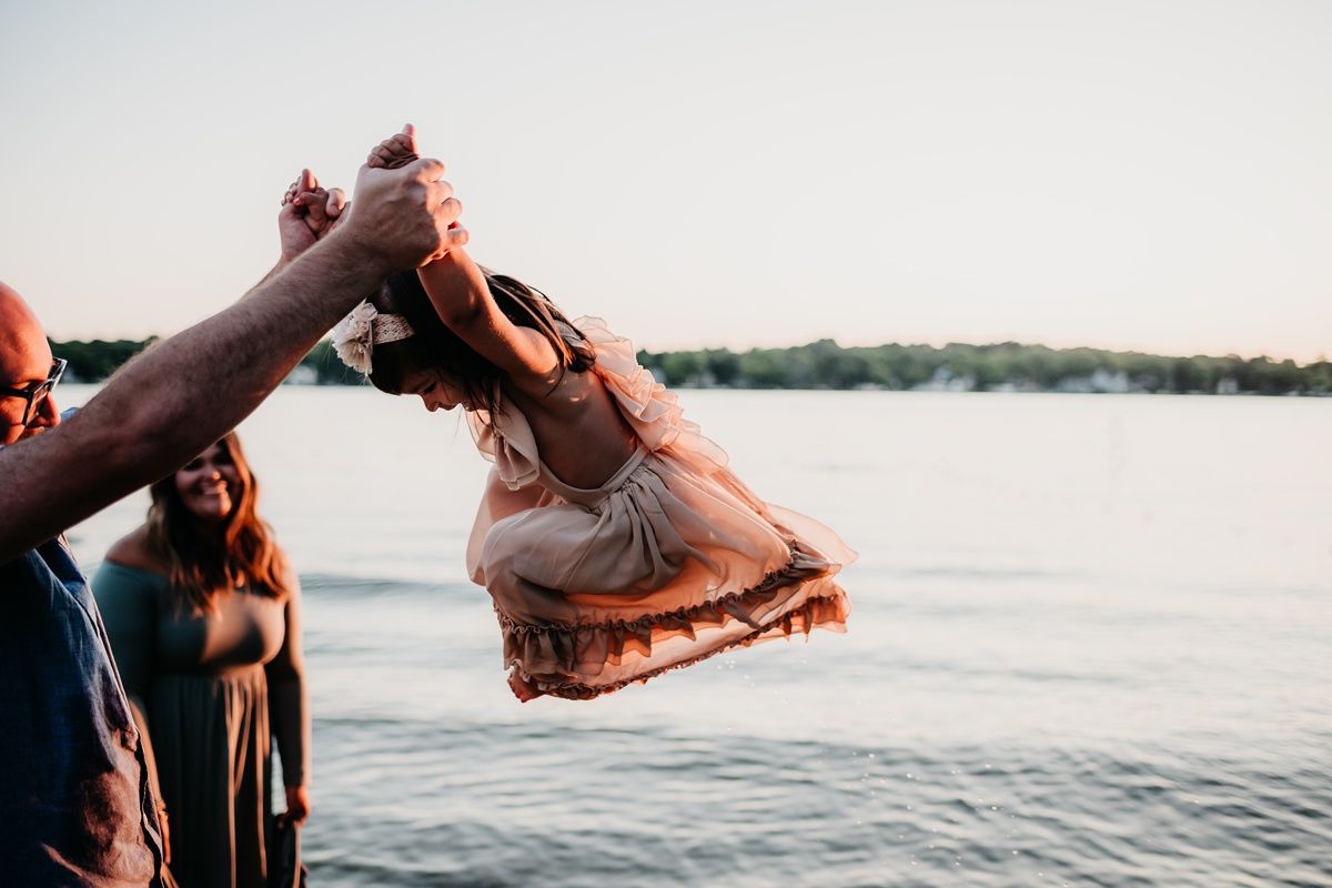 Playful moment by the lake as a small child is lifted into the air during sunset.