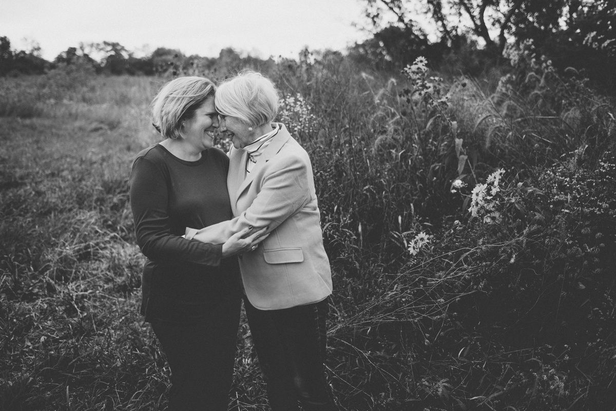 An intimate black and white portrait of two people embracing in a natural outdoor setting.
