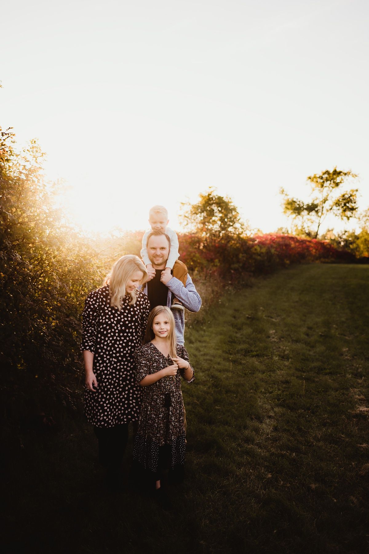 Family of four poses together in backlit golden sunset among trees.