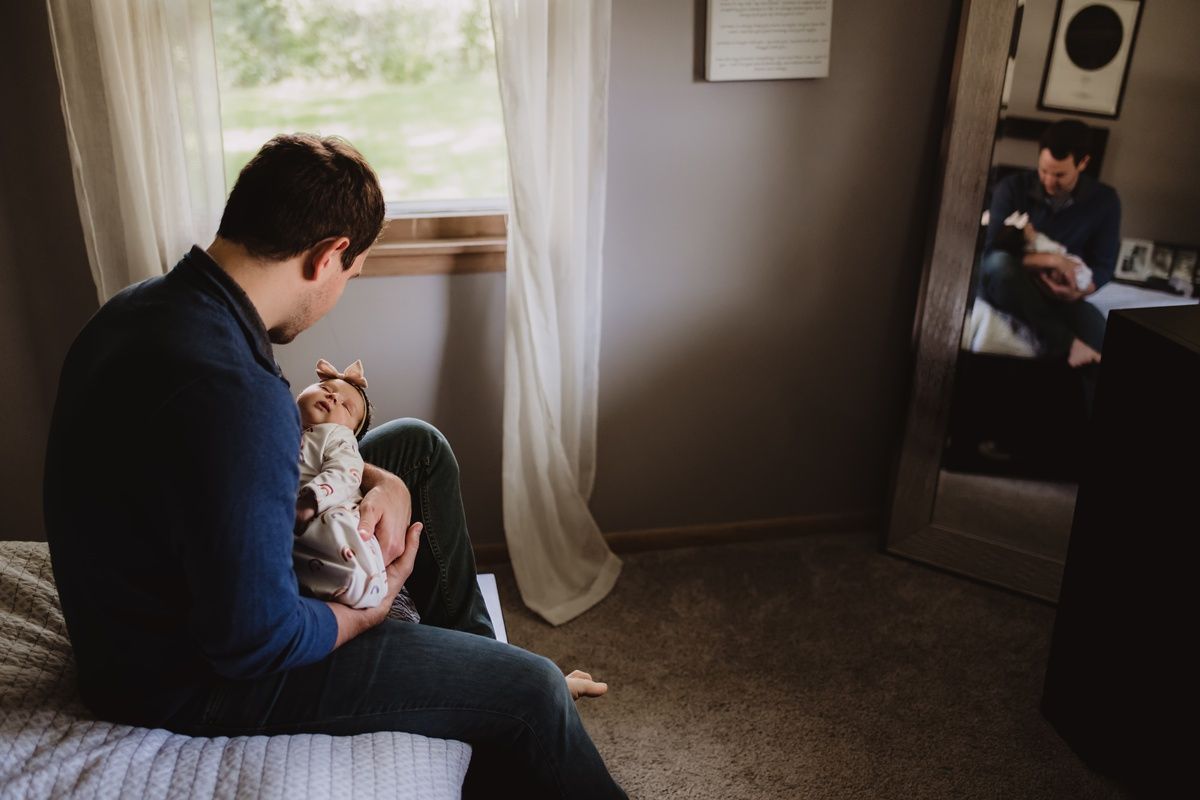 Quiet moment by a window as parent holds newborn in a dimly lit room.