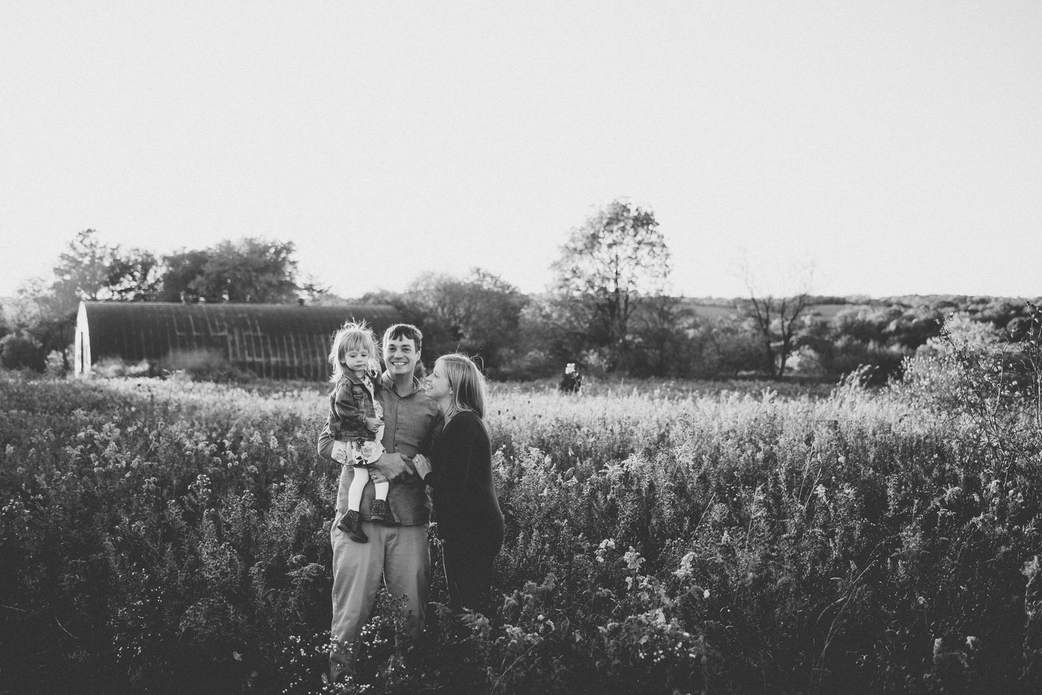 A black and white portrait of a family standing together in a wildflower meadow.