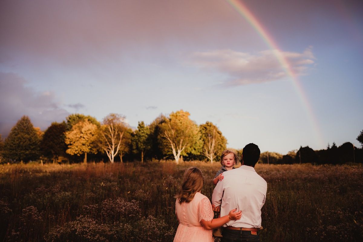 Couple sitting in field watching beautiful double rainbow in sunset sky.