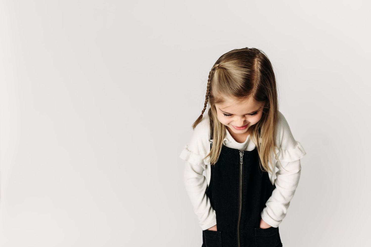 Child looking down while wearing black jumper dress with white long sleeve shirt.