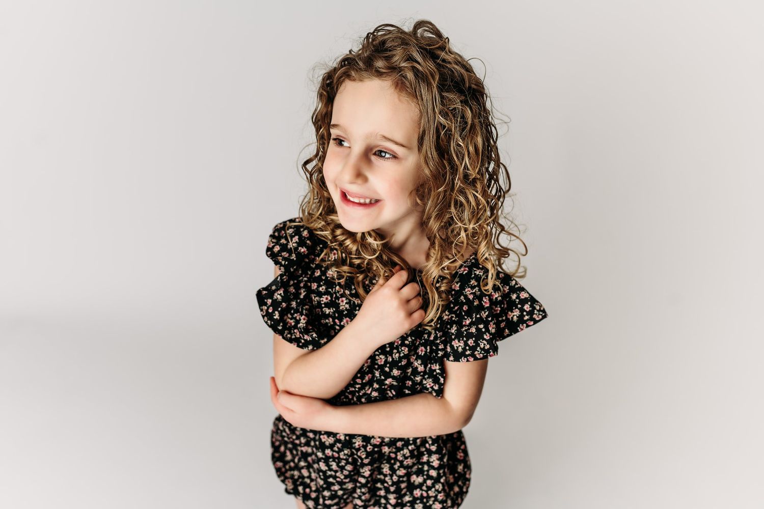 A child in a black floral outfit poses playfully on white background.