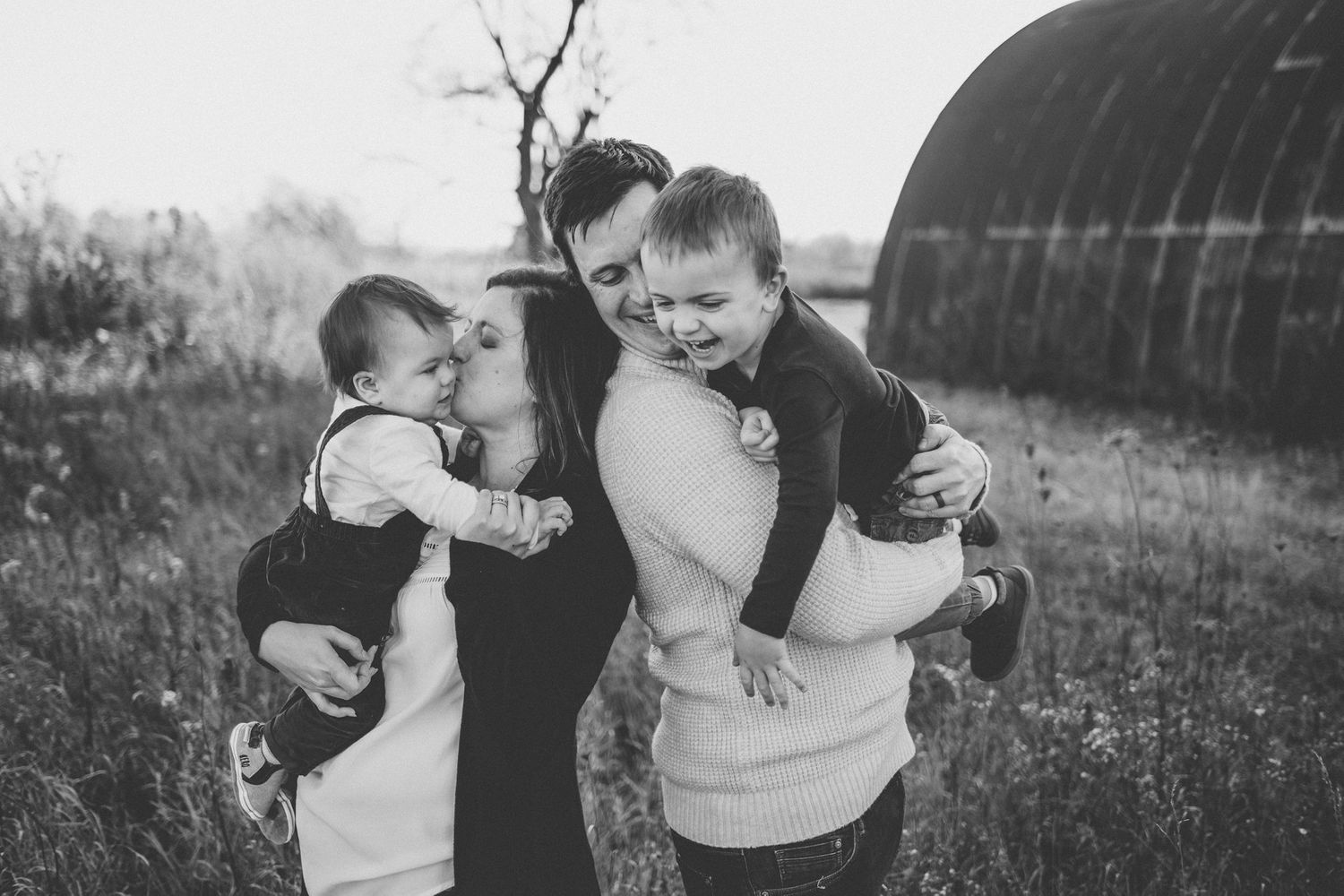 Black and white candid family photo outdoors with rustic barn setting.