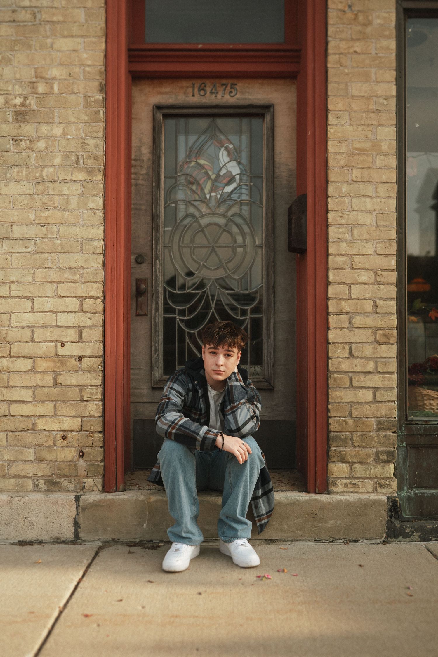 Person sitting on concrete steps outside brick building with decorative glass door.