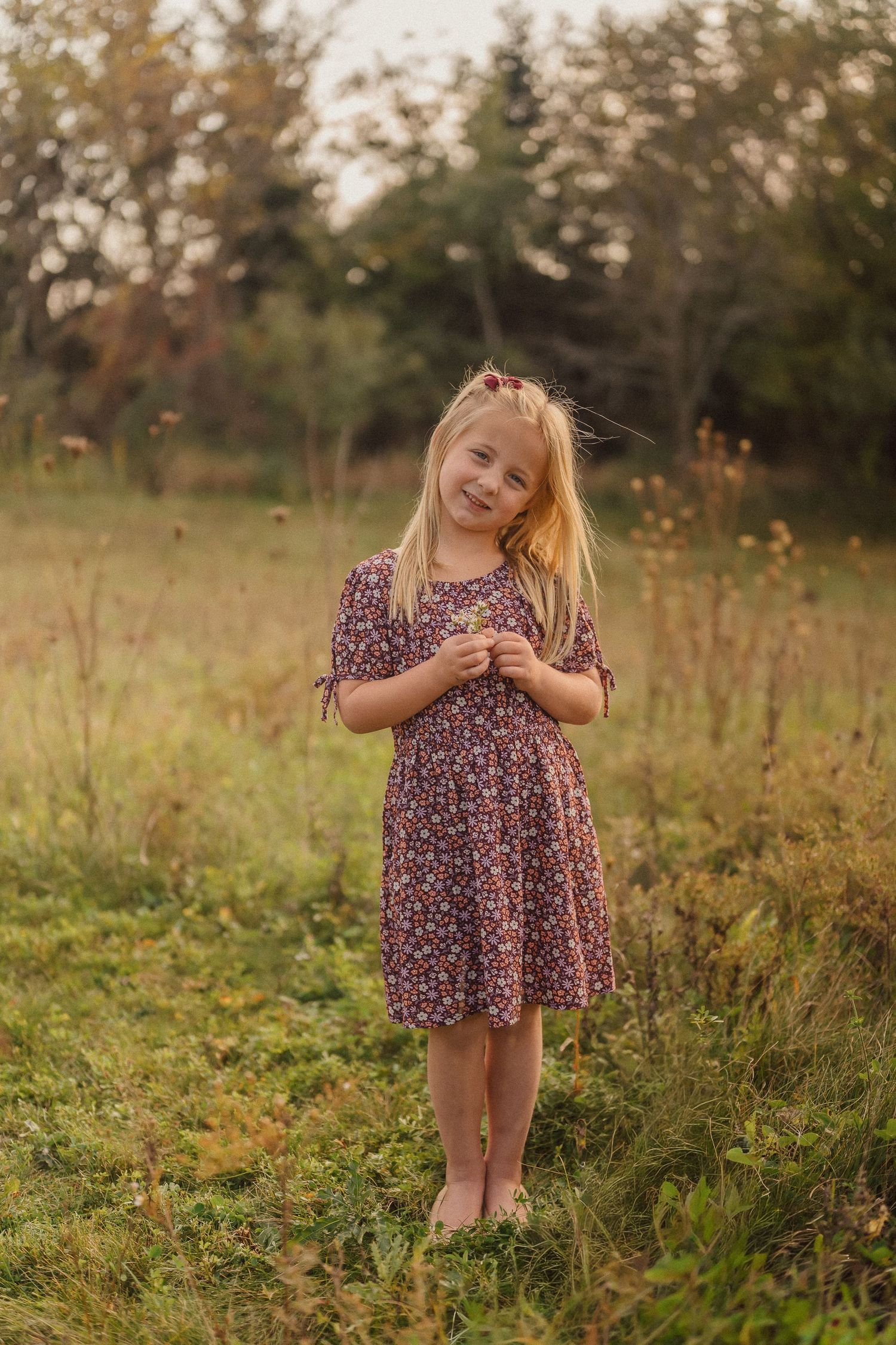 Young child in floral dress twirls playfully in a wildflower meadow at sunset.