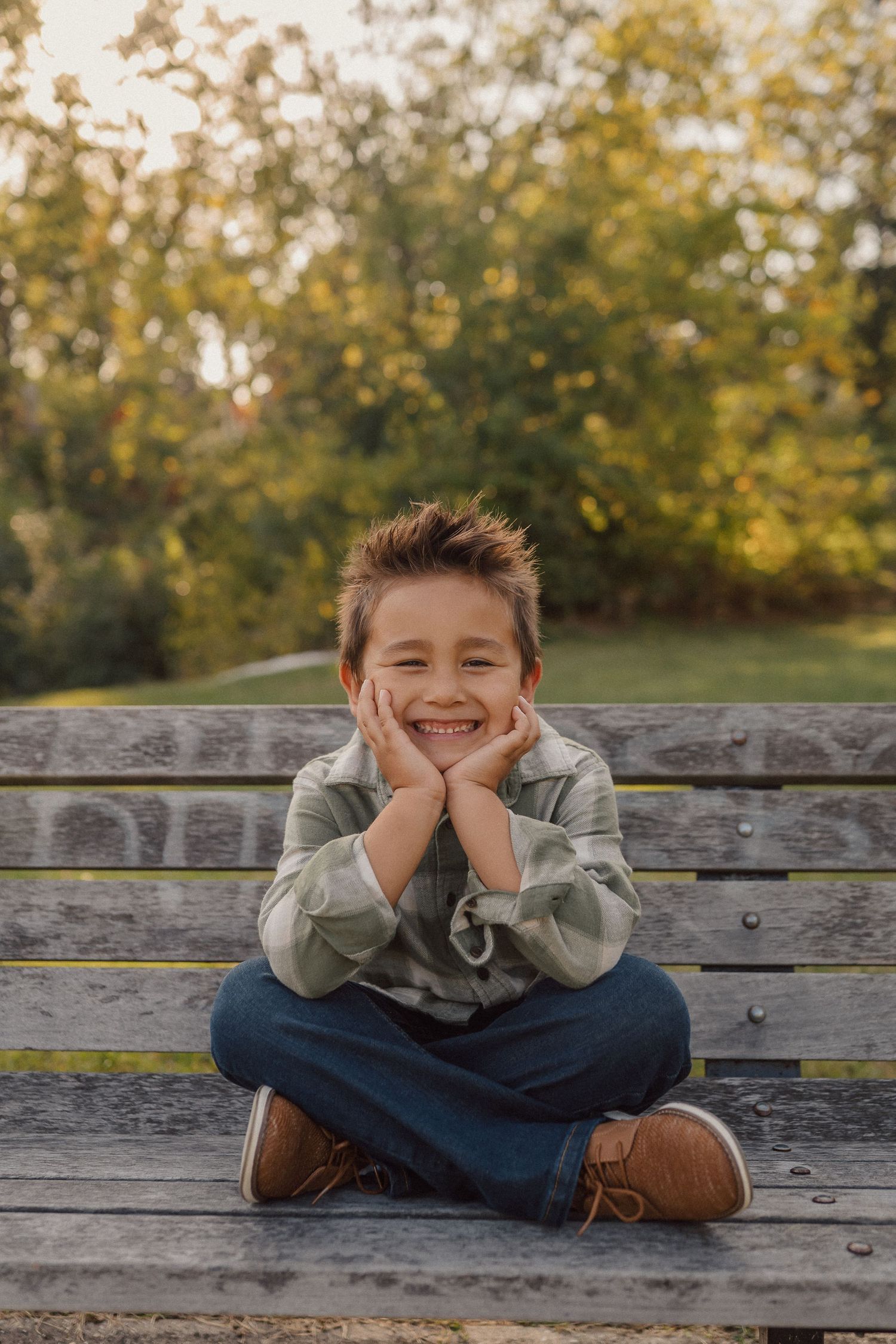 A child poses playfully on a wooden bench during a sunny autumn photoshoot.