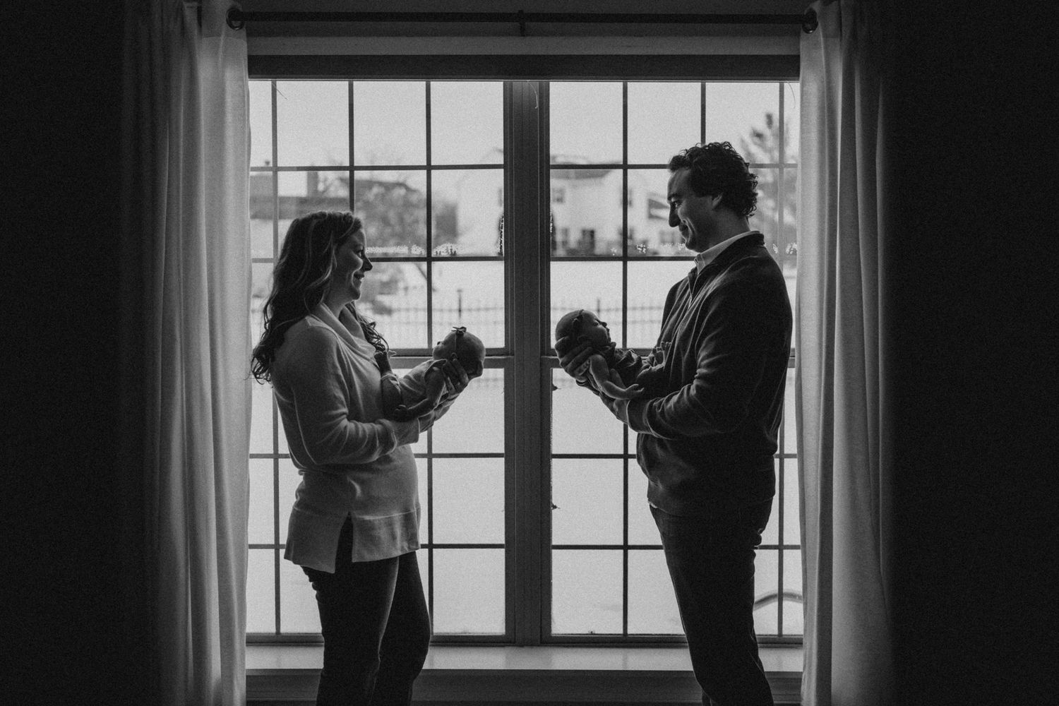 A silhouetted couple stands in front of a bright window having a conversation in black and white.