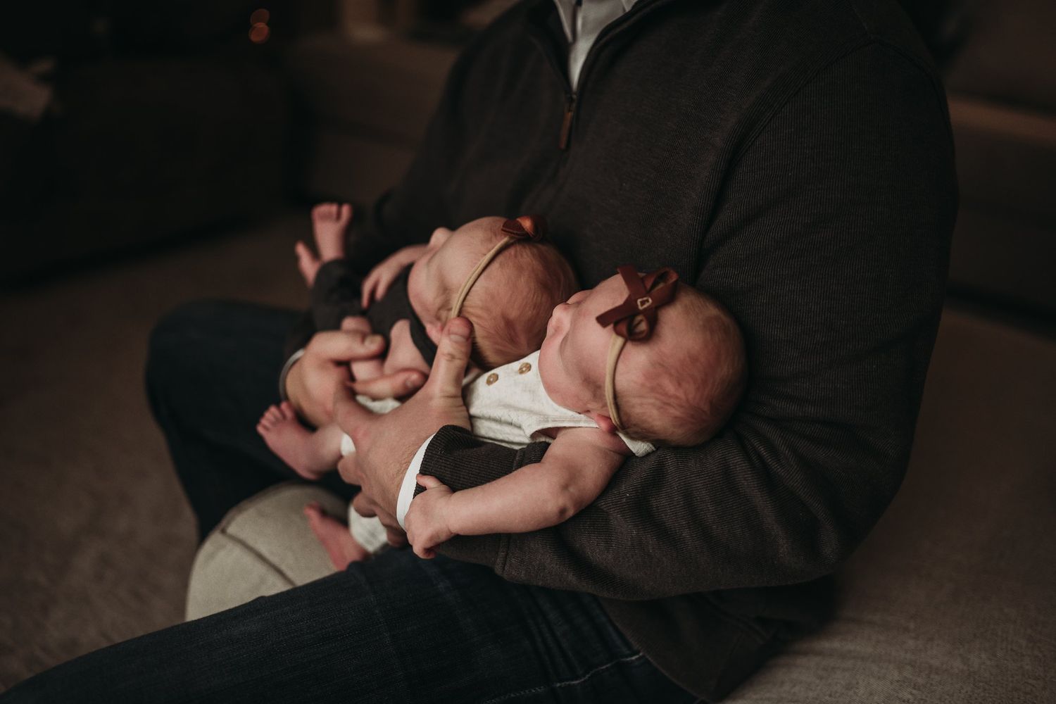 Parent sitting on couch gently holds peaceful sleeping newborn in casual home setting.