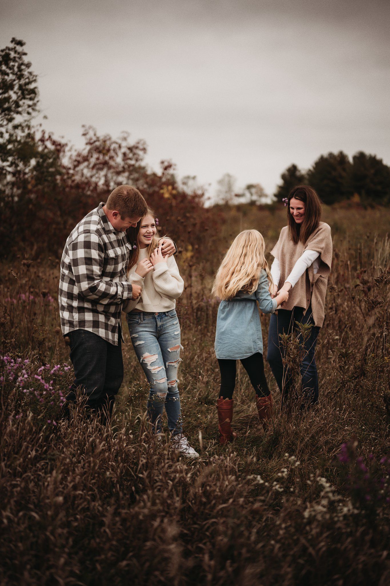 A family shares joyful laughter together in a rustic autumn field with purple wildflowers.