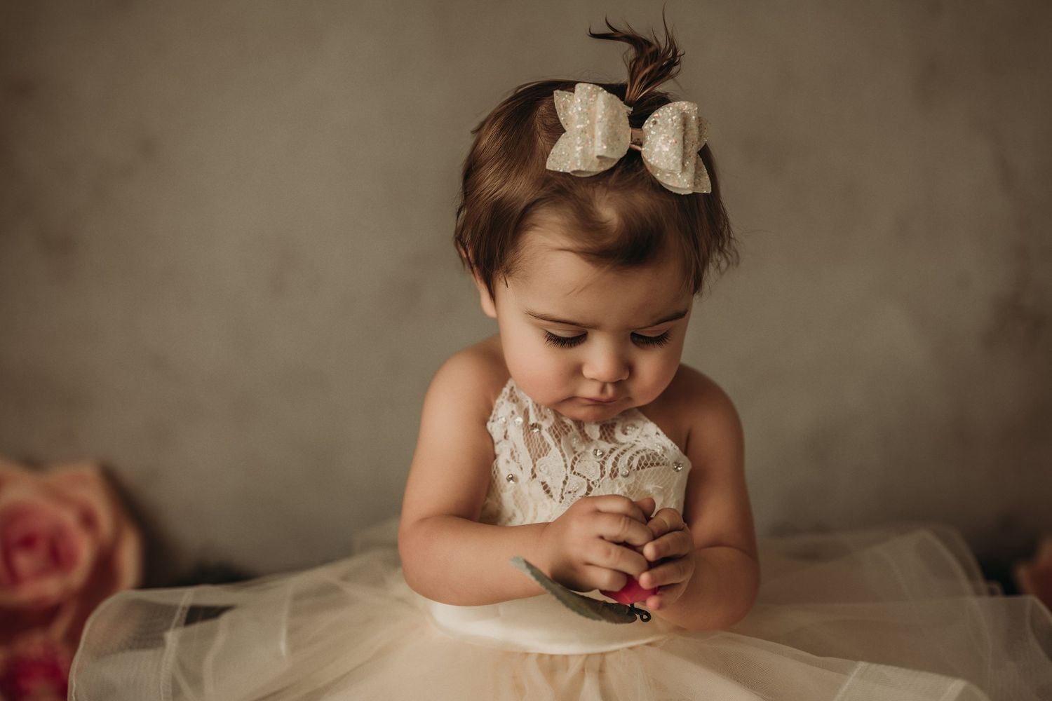 Adorable portrait with white tulle dress and bow against neutral background.