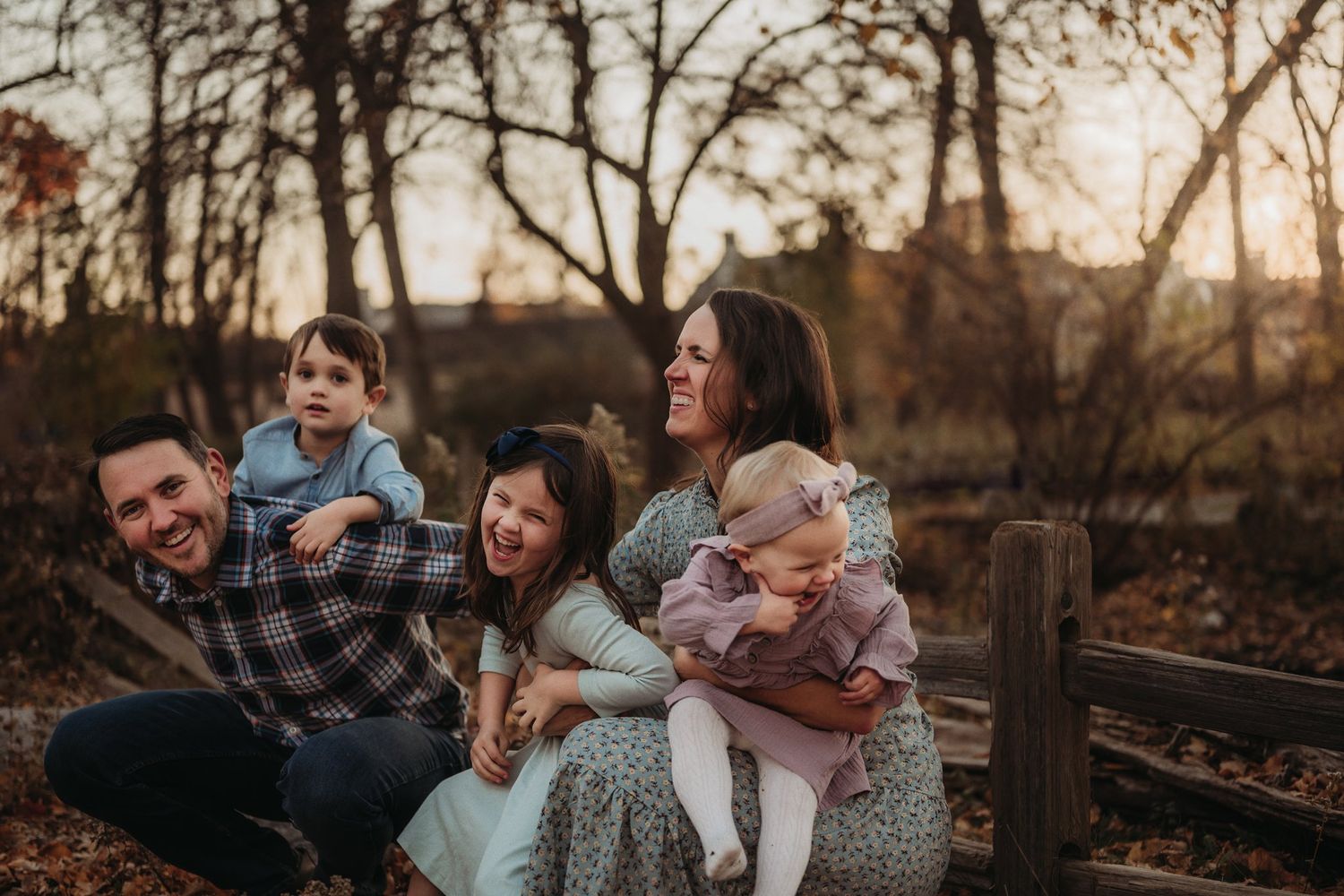 A joyful family moment captured on a rustic fence during golden hour in fall.