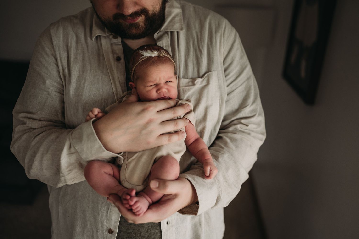 A person in a light colored shirt cradles a sleeping newborn against their chest.