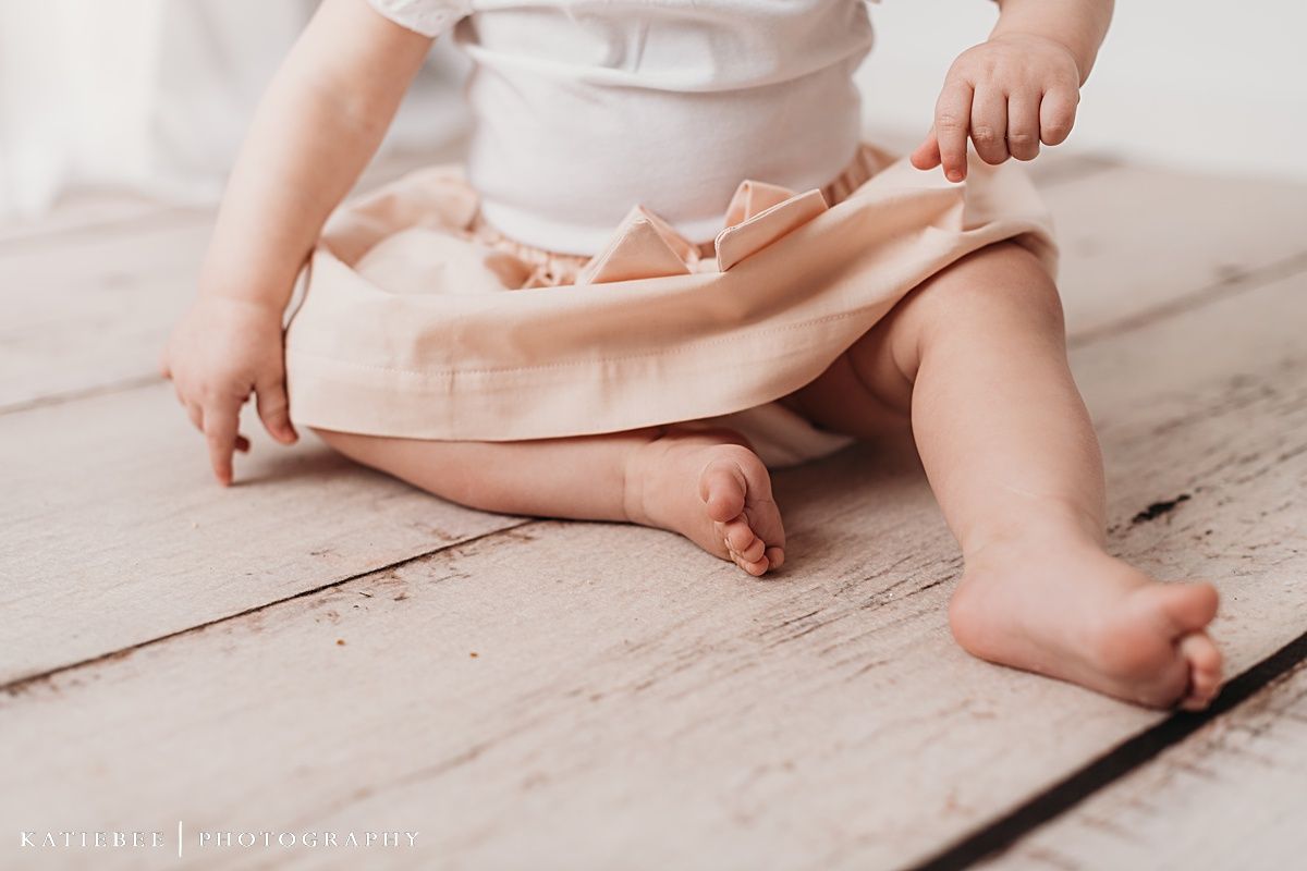 Baby in mint green outfit sitting on white floor with floral wreaths on wall.