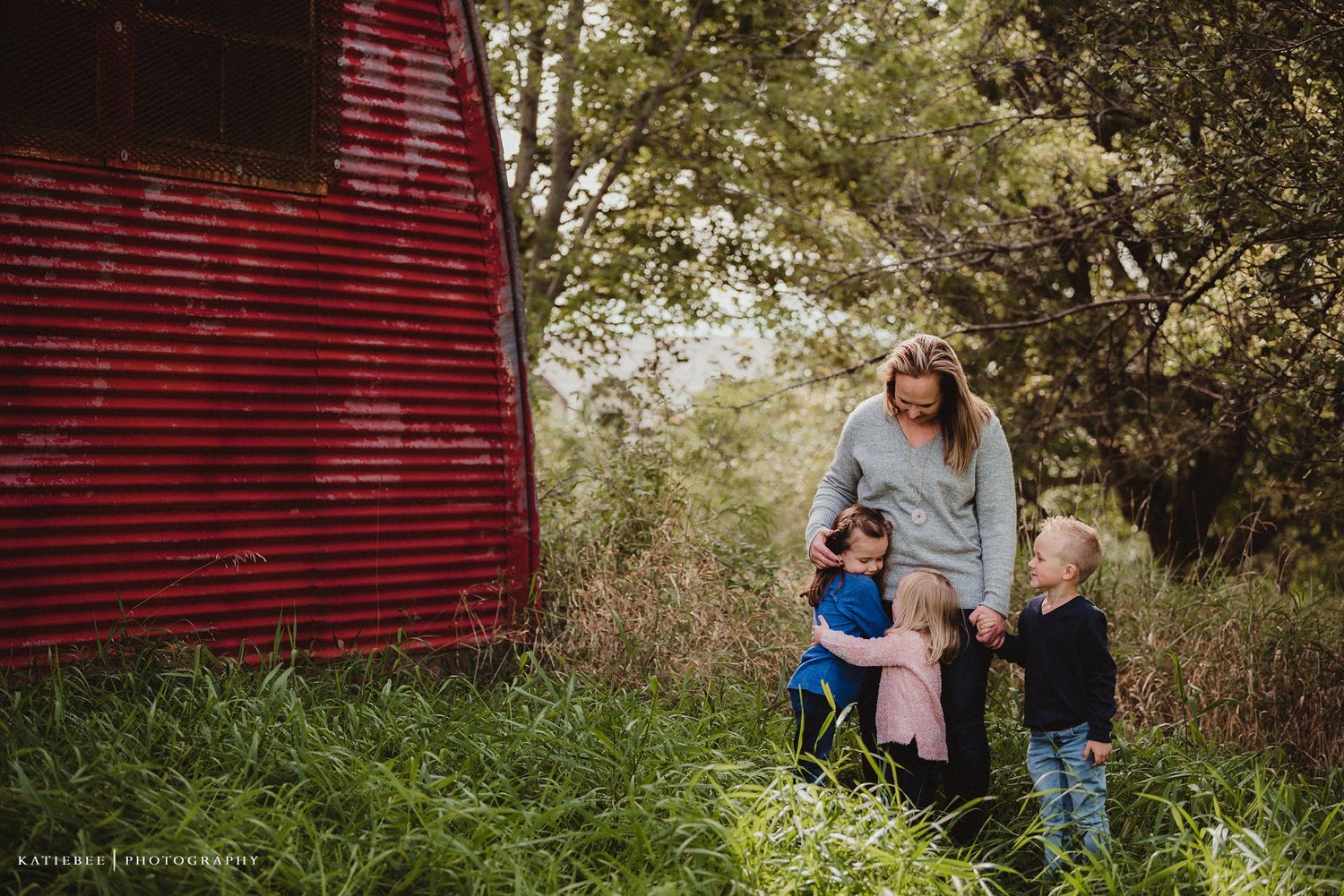 Family group standing together near a rustic red barn wall in a grassy field.