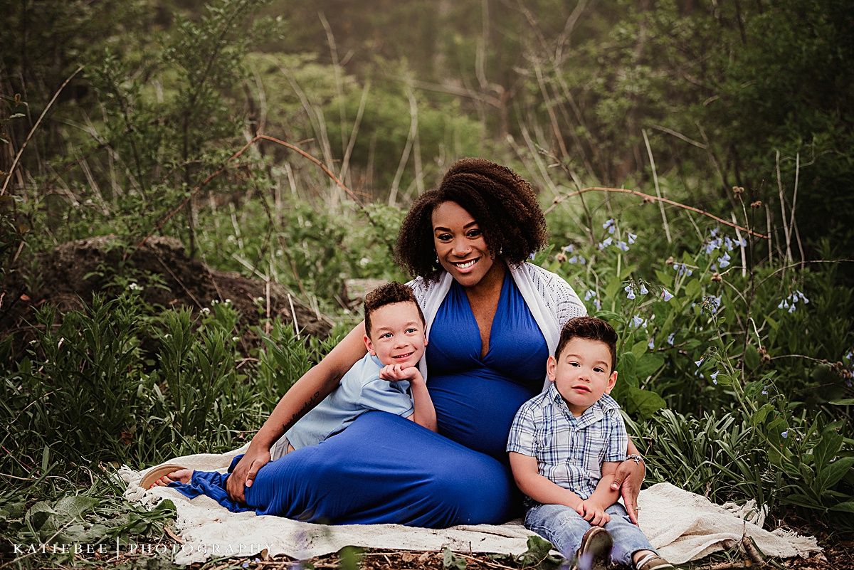 Family portrait outdoors showing joyful mother with children sitting on blanket among wildflowers.